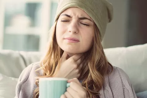 Frau mit Mütze und Teetasse, die sich an den Hals greift